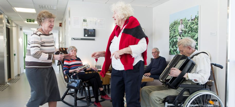 Bilde av to eldre damer som danser, og en eldre mann som spiller trekkspill