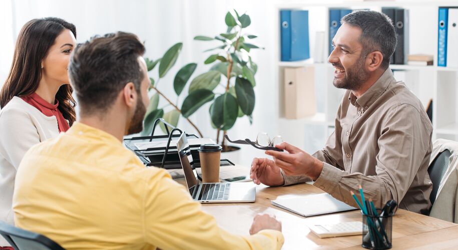 Vurderer du å starte egen bedrift? Nå kan du få etablererveiledning. Tre personer som sitter og snakker over et bord med en formell og lett tone